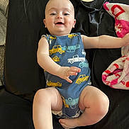 Rowan is registered to the contest to win money with this photo: baby, child, infant, smiling, blue_onesie, cars_pattern, black_background, blanket, pink_blanket, wooden_sign, six_months, happy, face, arms, legs, indoor, candid, cute, person, portrait