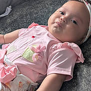 Isla joined the competition — help win amazing prizes! baby, infant, child, pink_clothing, headband, bow, couch, gray_fabric, puckered_lips, cute_expression, soft_skin, indoor, apparel, sitting_position, plush, small_arm, adorable, relaxed, portrait, closeup