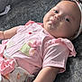 baby, infant, child, pink_clothing, headband, bow, couch, gray_fabric, puckered_lips, cute_expression, soft_skin, indoor, apparel, sitting_position, plush, small_arm, adorable, relaxed, portrait, closeup