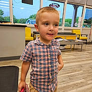 Christopher is registered to the contest to win money with this photo: boy, car_outside, casual_clothing, child, curious, daylight, floor, furniture, holding, indoor, khaki_shorts, person, plaid_shirt, short_hair, smile, standing, toy, waiting_room, window, yellow_chair