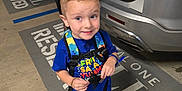 Christopher is registered to the contest to win money with this photo: adult, backpack, blue_shirt, boy, car, casual_clothing, child, concrete, footwear, gray_pants, hand, parking_lot, playful, reserved_parking, smile, standing, suv, tattoo, urban, vehicle