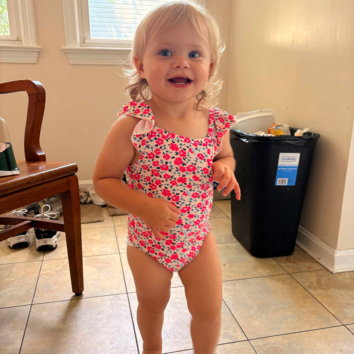 Kayliah joined the competition — help win amazing prizes! toddler, child, smiling, indoor, floor, tile, swimsuit, barefoot, hair, window, chair, trash_bin, shoes, home, person, happy, cute, walking, light, room