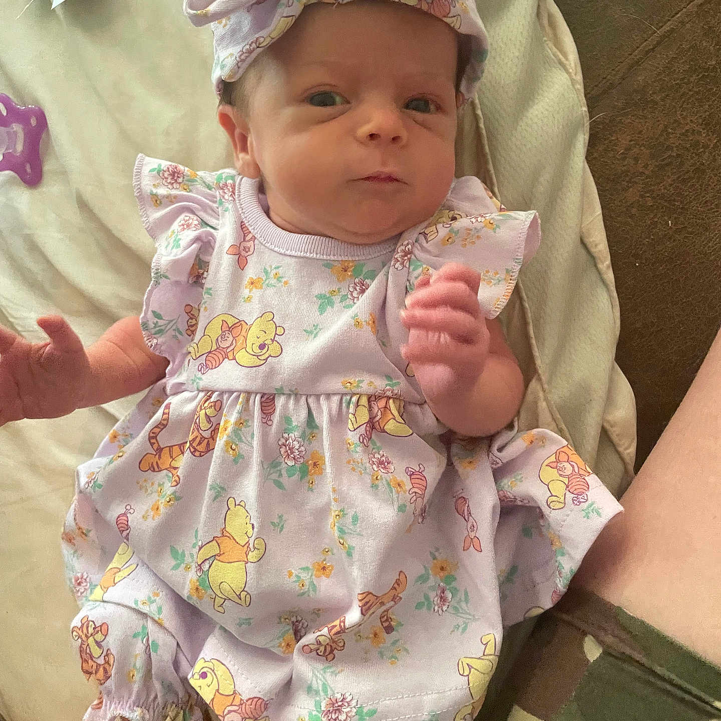 Mazzie is registered to the contest to win money with this photo: baby, camouflage, child, closeup, curious_expression, cute, face, hand, headband, indoors, infant, legs, lying_down, newborn, patterned_clothing, person, purple_outfit, shorts, soft_surface, winnie_the_pooh