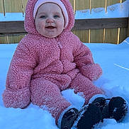 Kinsley joined the competition — help win amazing prizes! baby, child, snow, pink_suit, winter, outdoor, smiling, face, hat, boots, cold, fence, cuteness, sitting, warm_clothing, happy, infant, playful, seasonal, portrait