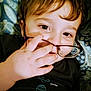 Odin is registered to the contest to win money with this photo: child, face, hand, glasses, brown_hair, eyes, smile, tshirt, pattern, blanket, lying_down, portrait, closeup, skin, fingers, casual, indoors, young, cute, expression