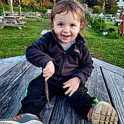 Odin joined the competition — help win amazing prizes! toddler, child, smiling, outdoor, grass, wooden_table, stick, sneakers, jacket, playground, nature, park, happy, person, casual_clothing, daylight, bench, trees, fun, cute
