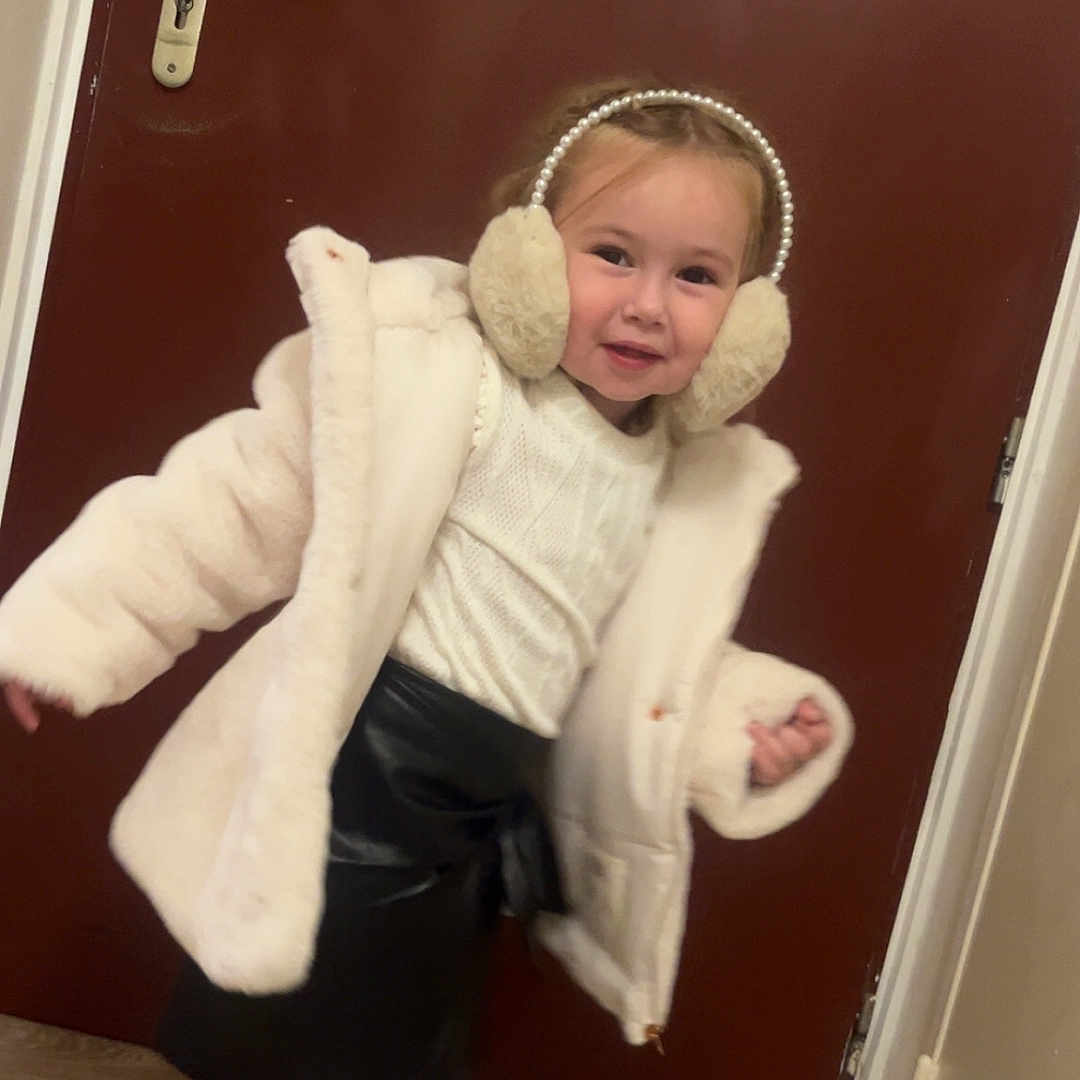 Lydiana participe au concours pour gagner de l'argent avec cette photo : black_skirt, child, cozy, cute, earmuffs, fashion, flooring, girl, happy, home, indoor, person, playful, portrait, smiling, standing, tights, white_jacket, winter_clothing, wooden_door