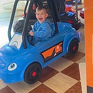 Giulyano a rejoint le concours — aidez-le/la à gagner de superbes lots ! child, toddler, toy_car, blue_car, smiling, indoor, shopping_mall, ride_on_toy, floor_tiles, happy, person, play, kid, vehicle, fun, casual_clothing, hoodie, plastic, wheels, entertainment