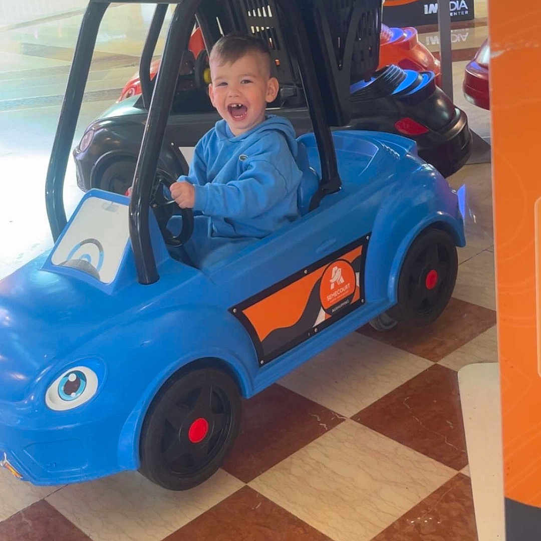 Giulyano a rejoint le concours — aidez-le/la à gagner de superbes lots ! blue_car, casual_clothing, child, entertainment, floor_tiles, fun, happy, hoodie, indoor, kid, person, plastic, play, ride_on_toy, shopping_mall, smiling, toddler, toy_car, vehicle, wheels