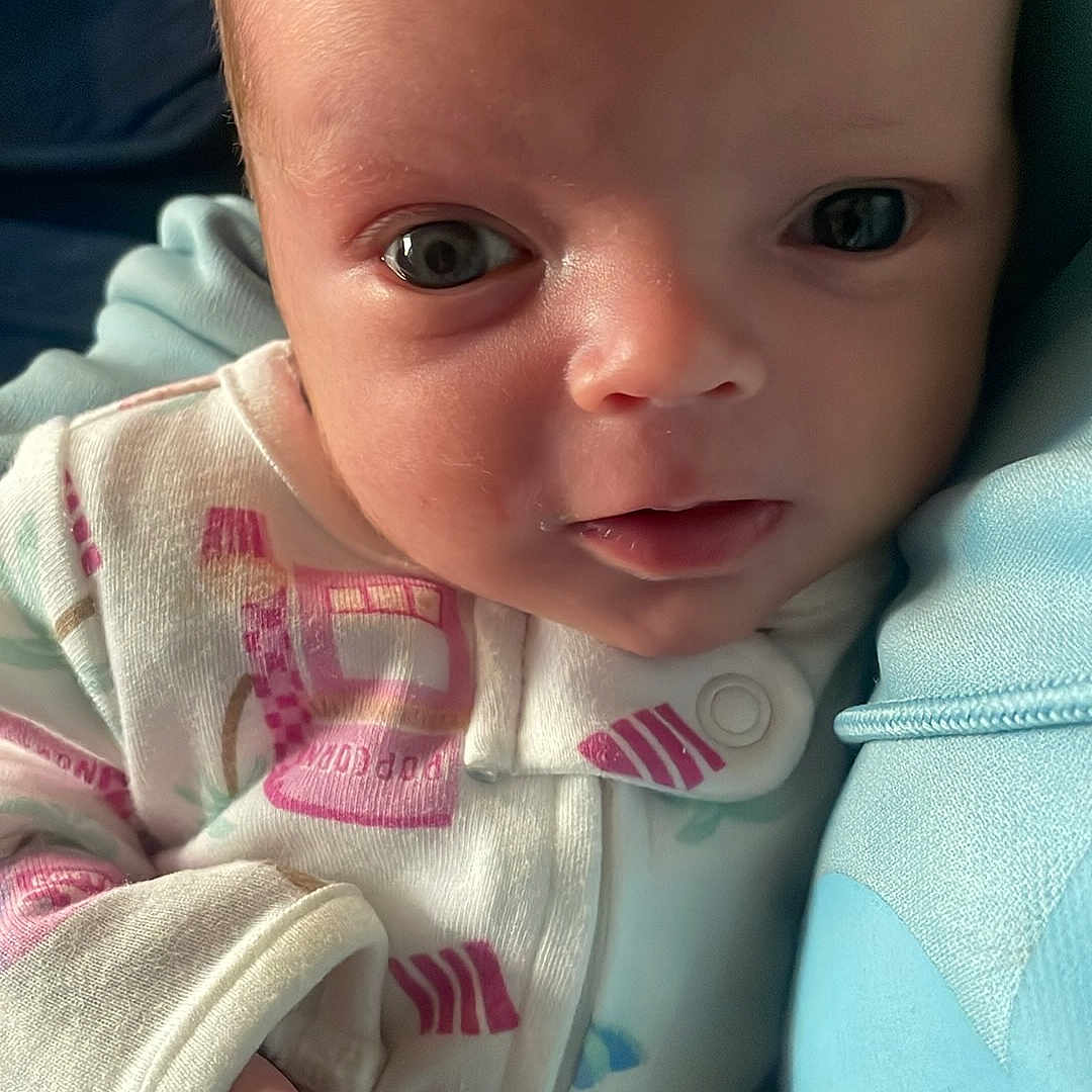 Serana is registered to the contest to win money with this photo: baby, infant, close_up, face, eyes, onesie, clothing, hand, skin, newborn, expression, portrait, young_child, cute, soft_lighting, indoor, comfort, blue, fabric, person