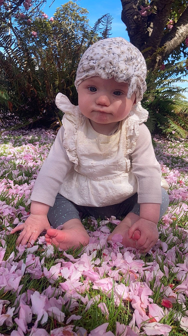 Alexis is registered to the contest to win money with this photo: baby, baby_toddler_clothing, botany, cap, dress, flower, grass, green, groundcover, happy, headwear, leaf, organ, people, people_in_nature, person, petal, photograph, pink, plant