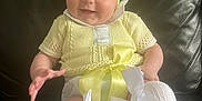 Aurora is registered to the contest to win money with this photo: baby, smiling, yellow_clothing, headband, bow, socks, white_socks, knitwear, couch, leather, indoor, child, cute, happy, portrait, seated, infant, apparel, fashion, person