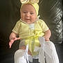 baby, smiling, yellow_clothing, headband, bow, socks, white_socks, knitwear, couch, leather, indoor, child, cute, happy, portrait, seated, infant, apparel, fashion, person