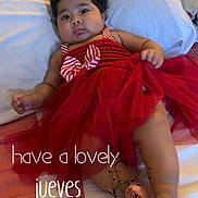Itzel joined the competition — help win amazing prizes! baby, child, infant, red_dress, portrait, lying_down, bed, bedroom, pillow, blanket, smiling, wide_eyed, dark_hair, cute, indoor, fashion, bow, striped_clothing, feet, text_overlay