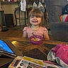 toddler, child, smile, cereal, bowl, spoon, table, wood, chair, armchair, living_room, furniture, indoors, household, tablet, magazine, clothing, person, happy, hair