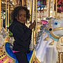 amusement_ride, black_clothing, carnival, carousel, child, colorful, curly_hair, entertainment, evening, fun, golden_pole, happy, horse, lights, outdoor, person, portrait, ride, smile, toy