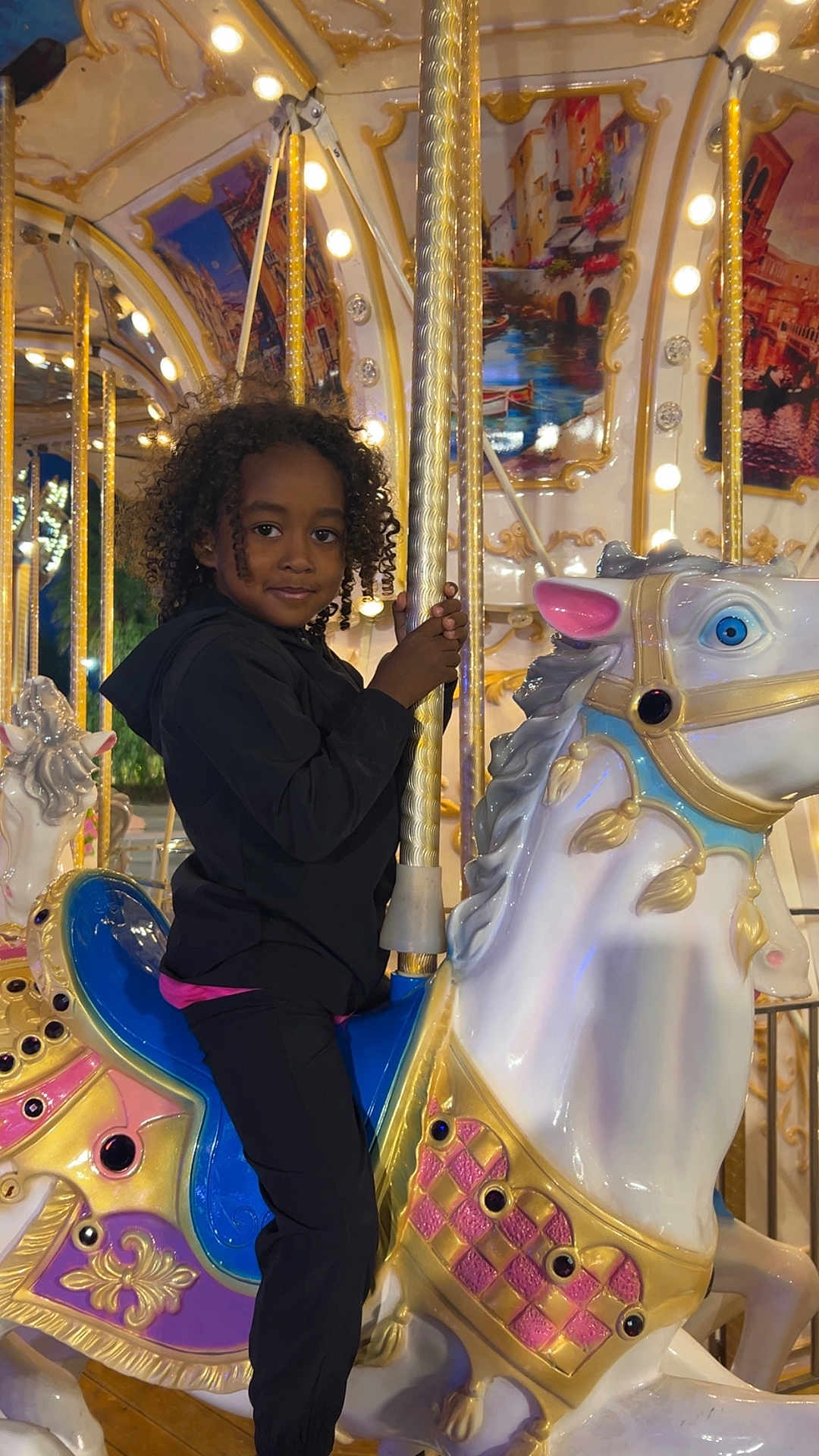 Kemil participe au concours pour gagner de l'argent avec cette photo : amusement_ride, black_clothing, carnival, carousel, child, colorful, curly_hair, entertainment, evening, fun, golden_pole, happy, horse, lights, outdoor, person, portrait, ride, smile, toy