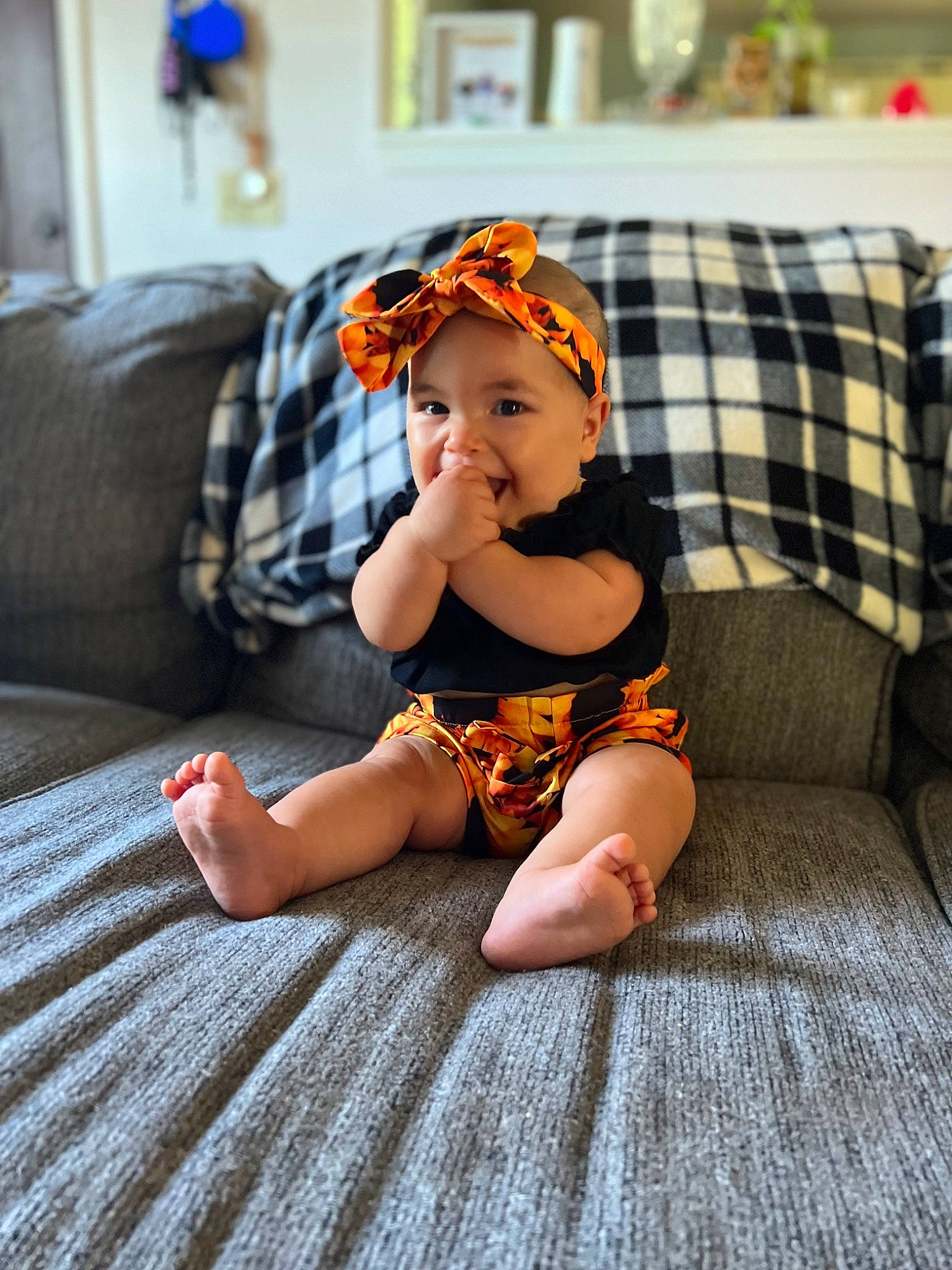 Adele is registered to the contest to win money with this photo: baby, baby_toddler_clothing, child, comfort, couch, eye, flash_photography, flooring, foot, happy, headwear, human_leg, living_room, orange, pattern, person, plaid, sitting, tartan, thigh