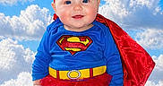 Zhelda Rose Swartz is registered to the contest to win money with this photo: baby, child, superhero_costume, cape, tutu, red_tights, blue_sky, clouds, fluffy_surface, smiling, portrait, cute, costume, red_headband, blue_eyes, sitting, infant, happy, outdoor, bright