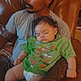 man, baby, sleeping, couch, tattoo, green_tshirt, indoor, arm, facial_hair, curly_hair, diaper, relaxing, seated, leather, comfort, peaceful, child, person, home, casual
