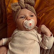 Léna participe au concours pour gagner de l'argent avec cette photo : baby, infant, pacifier, headband, knitted_bow, clothing, cushion, yellow, beige, texture, soft, lying_down, indoors, cute, child, portrait, peaceful, comfort, baby_girl, wrapped