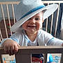 baby, child, hat, smile, playpen, toy, indoor, clothing, hand, floor_mat, happy, face, person, infant, blue, white, wood, cute, standing, cardigan