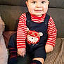 baby, child, smiling, sitting, striped_clothing, overalls, bear_design, couch, blanket, indoor, happy, face, hands, feet, socks, striped_socks, furniture, young_child, portrait, casual
