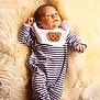 baby, infant, striped_clothing, onesie, bib, bear_patch, lying_down, fluffy_blanket, cream_color, soft_texture, newborn, cute, portrait, indoors, small_hands, face, head, footed_pajamas, cozy, sleepwear