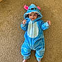 baby, blue_onesie, carpet, child, costume, cute, face, feet, floor, hood, indoors, infant, laying_down, looking_at_camera, monster_costume, person, plush, smiling, toy_like, young_child
