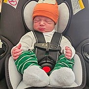 Yeshua is registered to the contest to win money with this photo: baby, infant, car_seat, hat, orange_hat, green_pants, striped_pants, white_socks, sleeping, child, seatbelt, safety, cute, newborn, indoors, closeup, person, resting, headwear, car