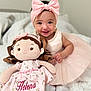 baby, child, doll, pink_dress, headband, bow, plush_toy, smile, jewelry, pearls, soft_toy, bed, blanket, indoor, cute, happy, person, portrait, toddler, sitting