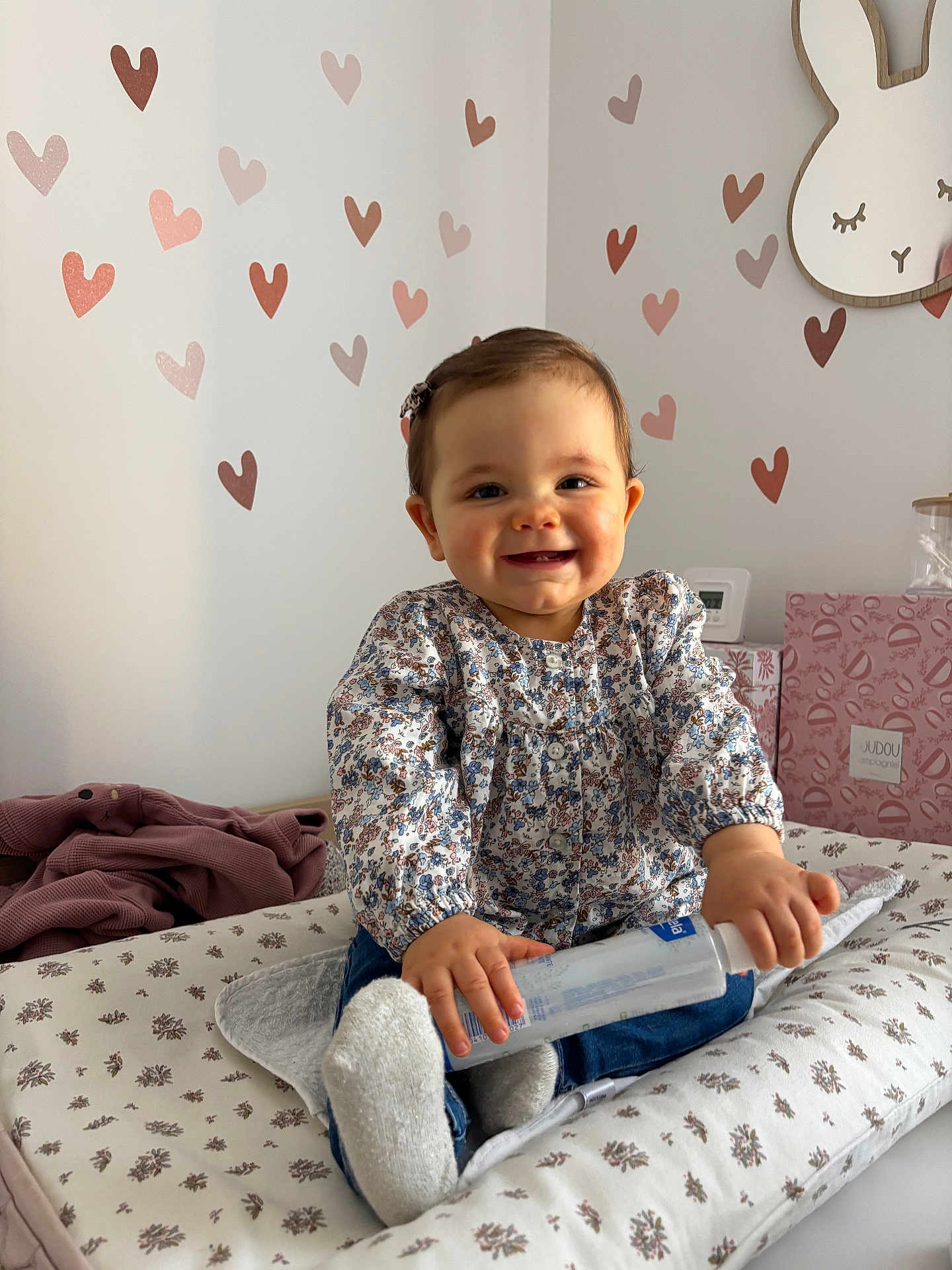 Lya a rejoint le concours — aidez-le/la à gagner de superbes lots ! baby, child, smiling, bottle, floral_clothing, hair_clip, socks, changing_pad, nursery, heart_wall_decals, bunny_wall_art, pink, brown, indoor, cute, happy, infant, sitting, patterned, toy