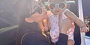 Celina is registered to the contest to win money with this photo: woman, baby, sunglasses, outdoor, car, trees, sunlight, headband, clothing, holding, smiling, person, cute, accessories, fashion, portrait, nature, casual, playful, family