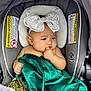 baby, child, car_seat, headband, bow, green_fabric, hand, face, infant, seat, blanket, cute, portrait, indoors, clothing, sitting, person, young_child, thoughtful, closeup
