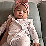 Celina is registered to the contest to win money with this photo: baby, child, infant, pink_bow, headband, floral_onesie, couch, hand, indoors, cute, portrait, seated, comfortable, skin, face, expression, clothing, furniture, person, young