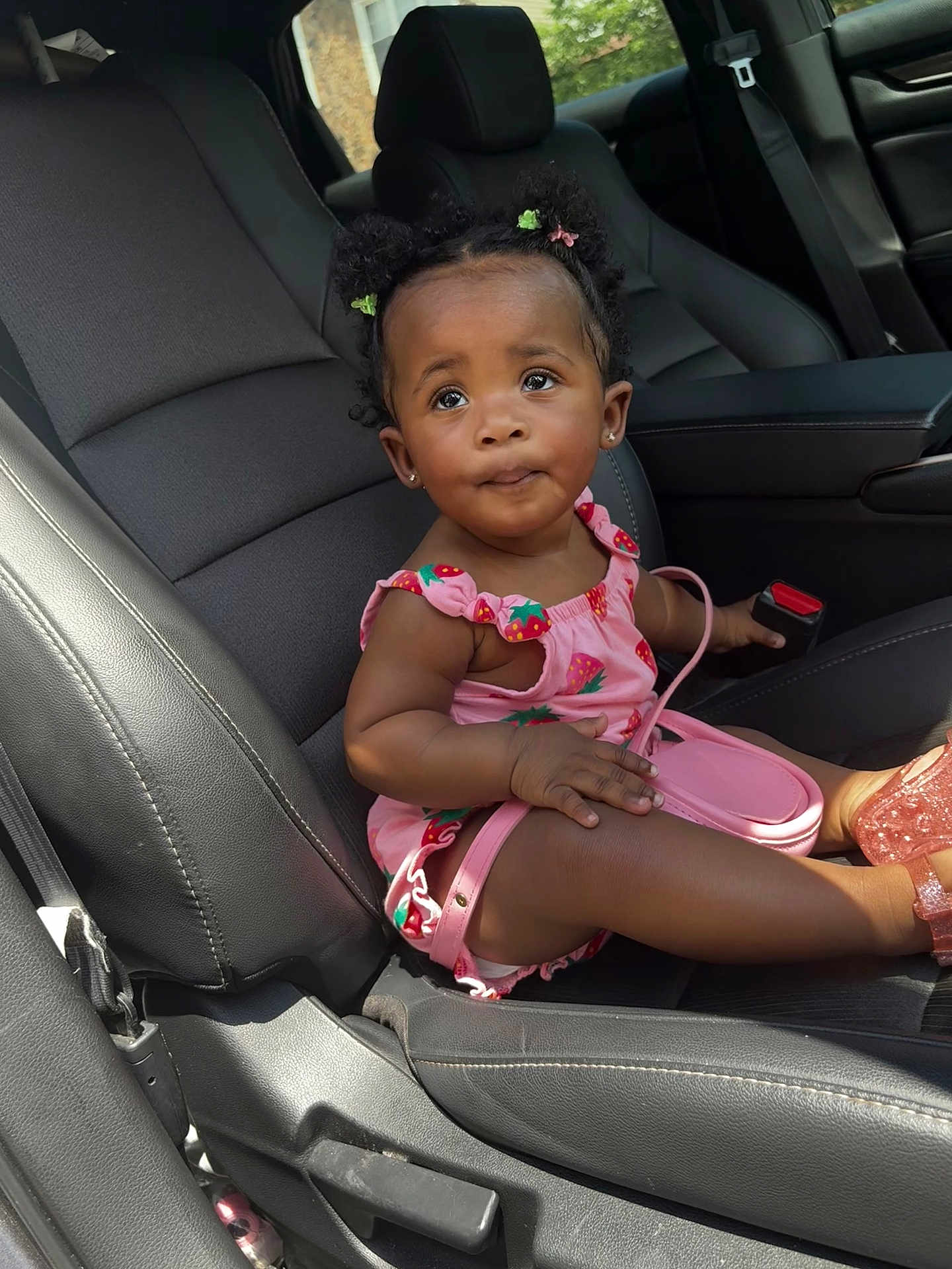 Reign joined the competition — help win amazing prizes! child, toddler, car_seat, pink_clothing, strawberry_pattern, purse, hair_buns, hair_clips, curious_expression, car_interior, black_leather_seat, seatbelt, footwear, pink_shoes, portrait, sitting, cute, baby, young_child, indoor