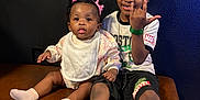 Reign is registered to the contest to win money with this photo: baby, bench, child, curly_hair, family, floor, happy, indoor, leather_bench, marvel, pink_bows, playful, portrait, shorts, sitting, smiling, socks, tshirt, two_children, wall