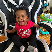 Reign joined the competition — help win amazing prizes! baby, child, smile, happy, sitting, red_shirt, black_pants, gray_socks, gaming_chair, curly_hair, earrings, indoor, floor, toys, walker, furniture, person, expression, home, wooden_floor