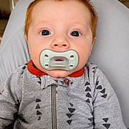 Emry joined the competition — help win amazing prizes! baby, pacifier, red_hair, onesie, gray_clothing, indoor, child, face, portrait, young_child, sitting, cozy, cute, head, expression, patterned_clothing, infant, person, closeup, casual