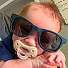 Emry is registered to the contest to win money with this photo: baby, pacifier, sunglasses, hand, face, closeup, infant, skin, hair, person, child, cute, relaxed, indoors, portrait, expression, casual, young, comfort, home