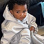 toddler, child, curly_hair, white_sneakers, hoodie, sweatpants, carpet, rug, knitted_hat, living_room, couch, black_couch, earrings, indoor, casual_clothing, sitting, person, cute, young_child, curious