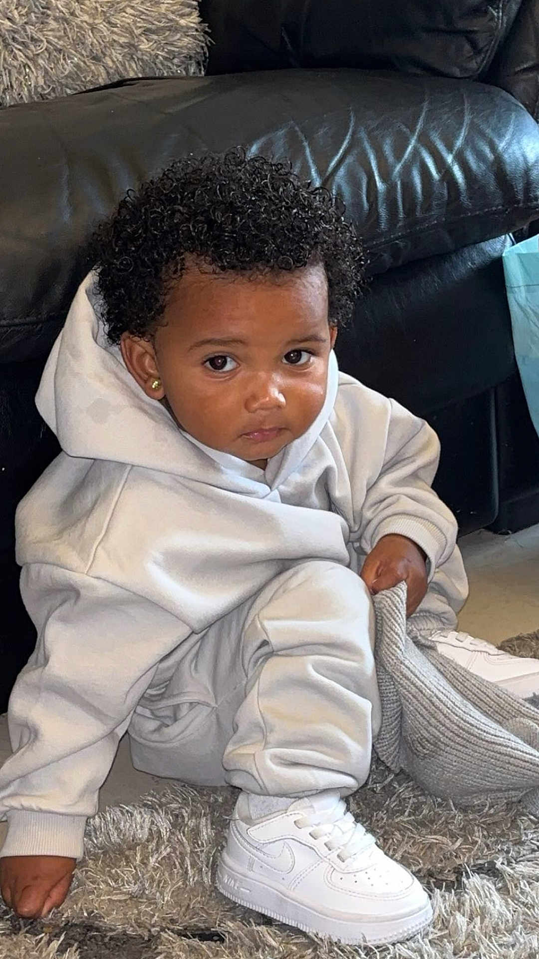 Rayne joined the competition — help win amazing prizes! toddler, child, curly_hair, white_sneakers, hoodie, sweatpants, carpet, rug, knitted_hat, living_room, couch, black_couch, earrings, indoor, casual_clothing, sitting, person, cute, young_child, curious