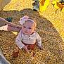 Cova is registered to the contest to win money with this photo: baby, child, corn, grain, toy_truck, flower_headband, tattoo, arm, clothing, sitting, yellow, metal_container, sunlight, outdoor, play, serious_expression, infant, small_toys, texture, casual