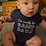 Mylo is registered to the contest to win money with this photo: baby, infant, child, onesie, blue_clothing, sitting, bed, hand_holding, curious, indoor, wooden_chair, face, feet, photograph, person, home, furniture, expression, football_graphic, cute