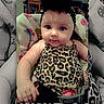 baby, infant, child, portrait, sitting, stroller, leopard_print, animal_print, dress, headband, dark_hair, wide_eyes, face, hands, indoor, furniture, blanket, cushion, colorful, photograph