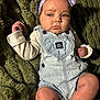baby, child, infant, headband, bow, denim_overalls, clothing, blanket, green_background, skin, face, legs, hand, portrait, indoor, cute, expression, young, person, sitting