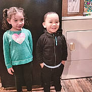 Jeffrey is registered to the contest to win money with this photo: child, kids, indoor, standing, smiling, clothing, sweater, hoodie, boots, floor, wood_floor, appliance, kitchen, box, curly_hair, boy, girl, portrait, happy, casual