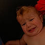 baby, bare_shoulders, child, closeup, curly_hair, dark_background, distress, emotion, expression, face, head, indoor, infant, person, portrait, red_fabric, skin, skin_tone, unhappy, young