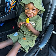 Ezra is registered to the contest to win money with this photo: child, toddler, smile, green_clothing, hat, car_seat, toy, yellow_object, happy, person, seat, interior, car, footwear, socks, cute, portrait, kid, seatbelt, vehicle