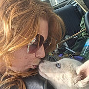 Simba is registered to the contest to win money with this photo: person, dog, close_up, red_hair, sunglasses, car_interior, window, blue_eyes, affection, nose_to_nose, casual_clothing, seat, seatbelt, daylight, pet, animal, indoor, friendship, love, candid